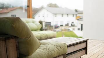 A wooden bench with green cushions, a wooden floor, and a view of a white house through a window.