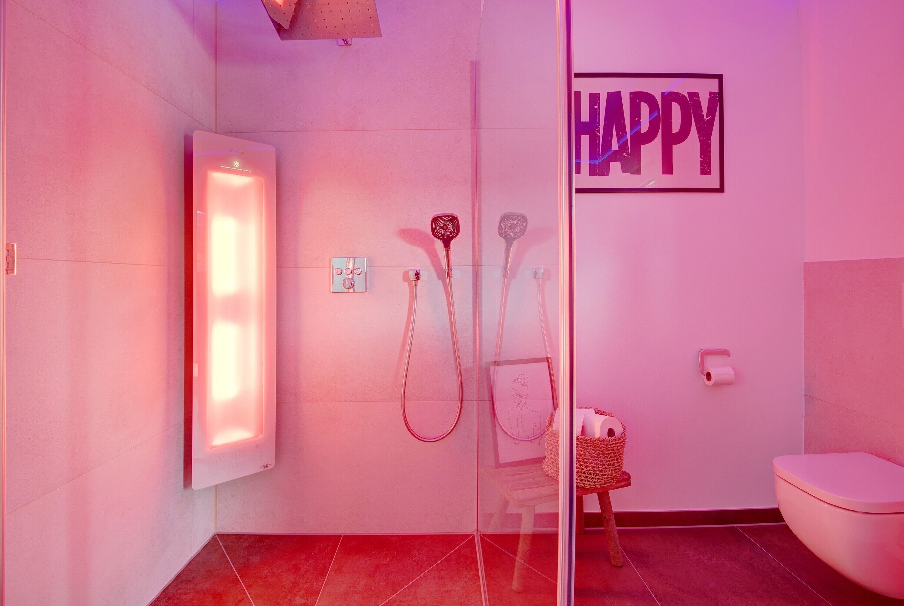 A bathroom with a glass shower enclosure, a toilet, a wall-mounted towel rack, and a 'HAPPY' sign.