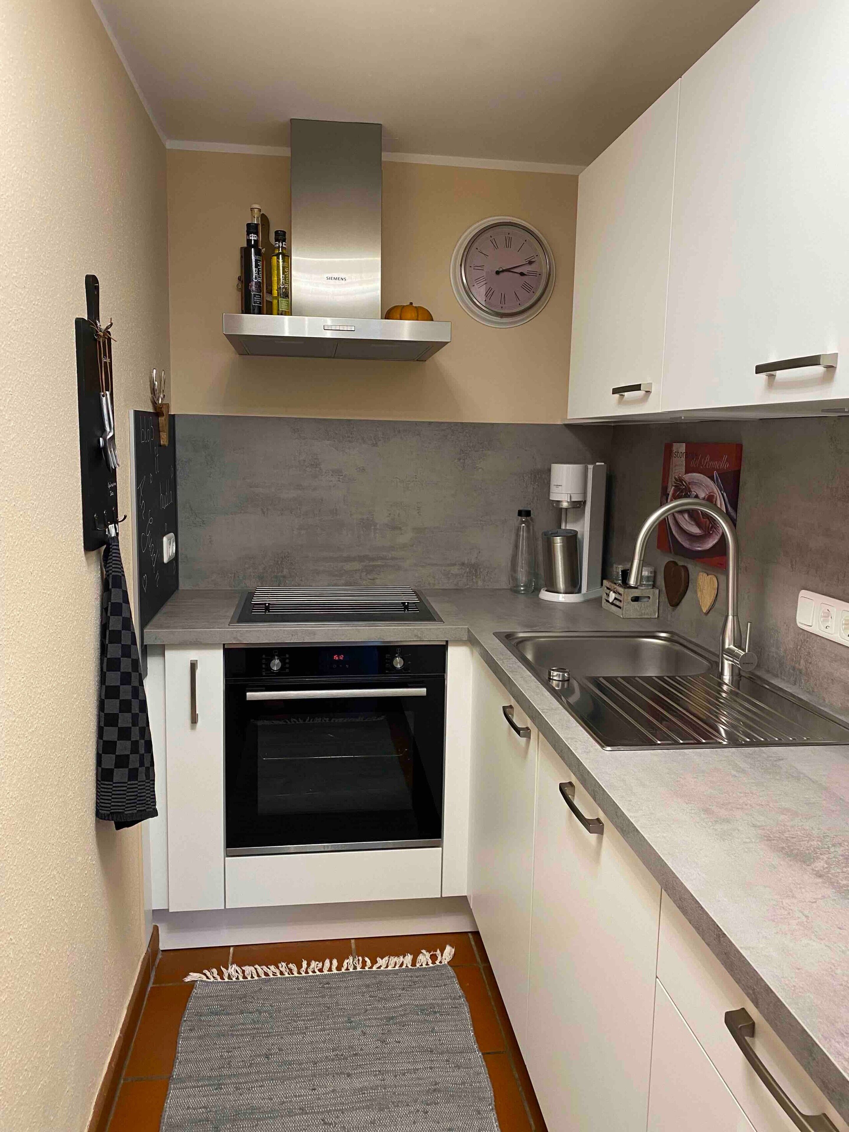 Una cucina compatta con forno integrato, cappa in acciaio inossidabile, orologio a parete e un piccolo lavello.