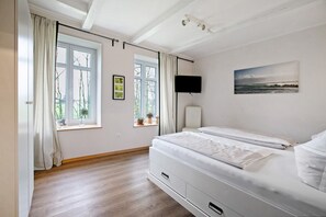 Un dormitorio con una cama, una ventana, un televisor y un cuadro en la pared.
