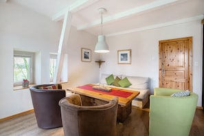 Una habitación con una mesa de madera, dos sillas, un sofá, una puerta de madera y una ventana con vistas.
