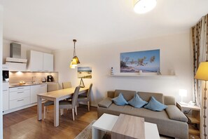 A modern kitchen with white cabinets, a dining table, and chairs. There is a sofa with cushions and a lamp on a side table.