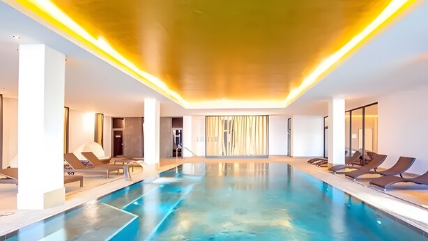 Une piscine intérieure moderne avec une eau d’un bleu cristallin, des chaises longues et un design contemporain au niveau du plafond.