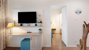Une chambre d’hôtel moderne équipée d’un téléviseur à écran plat, d’un bureau avec une lampe, d’une petite plante et d’un élément décoratif en bois.