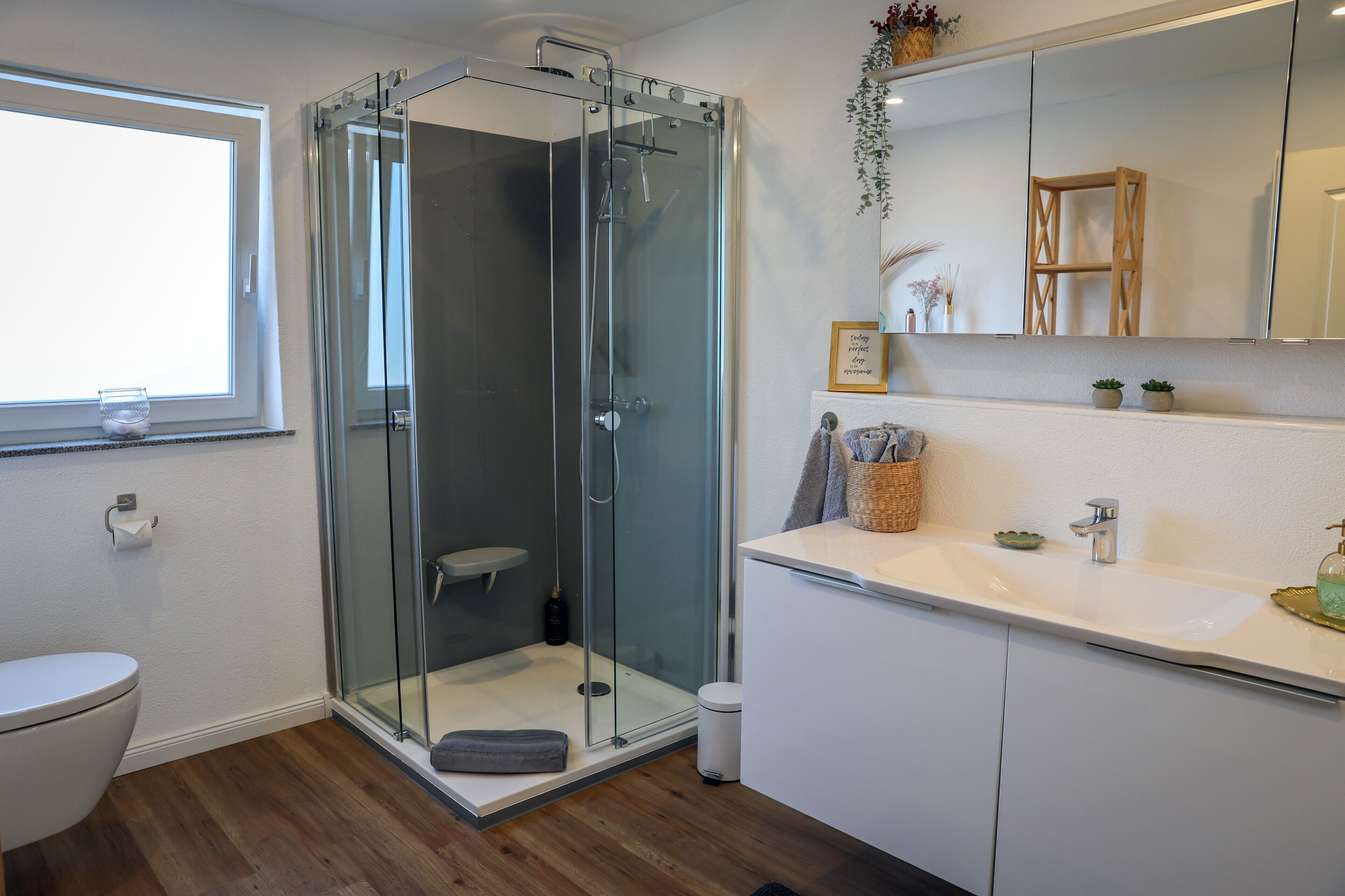 Ein modernes Badezimmer mit einer Duschkabine, einer Toilette und einem Waschbecken mit Spiegel darüber.