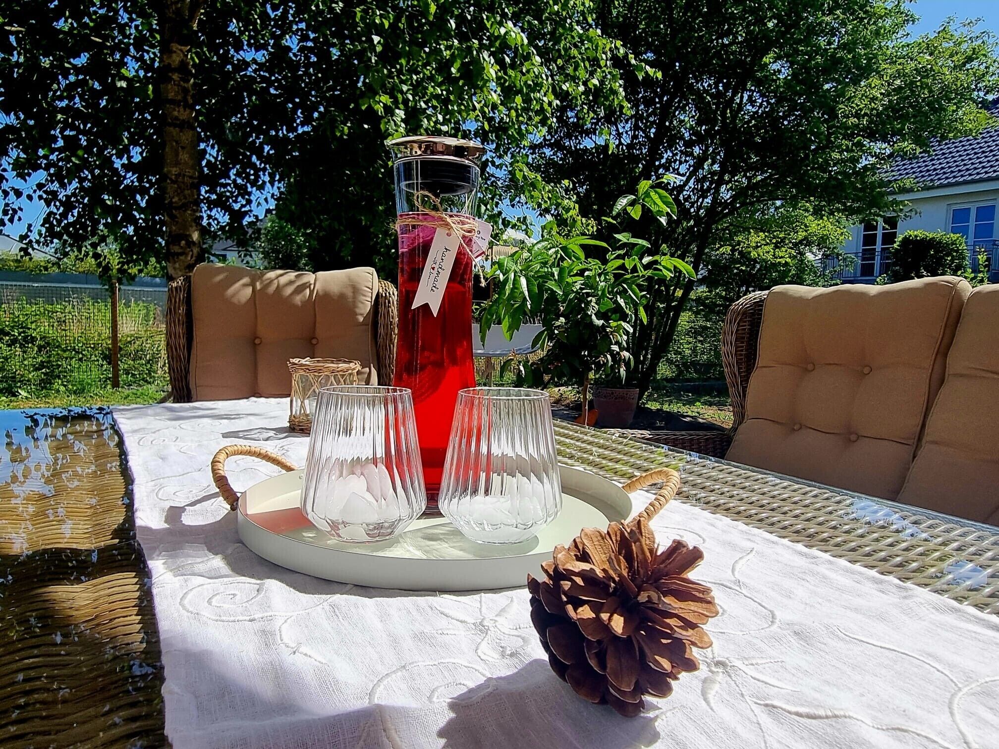 An outdoor table with a glass pitcher, glasses, and a pine cone.
