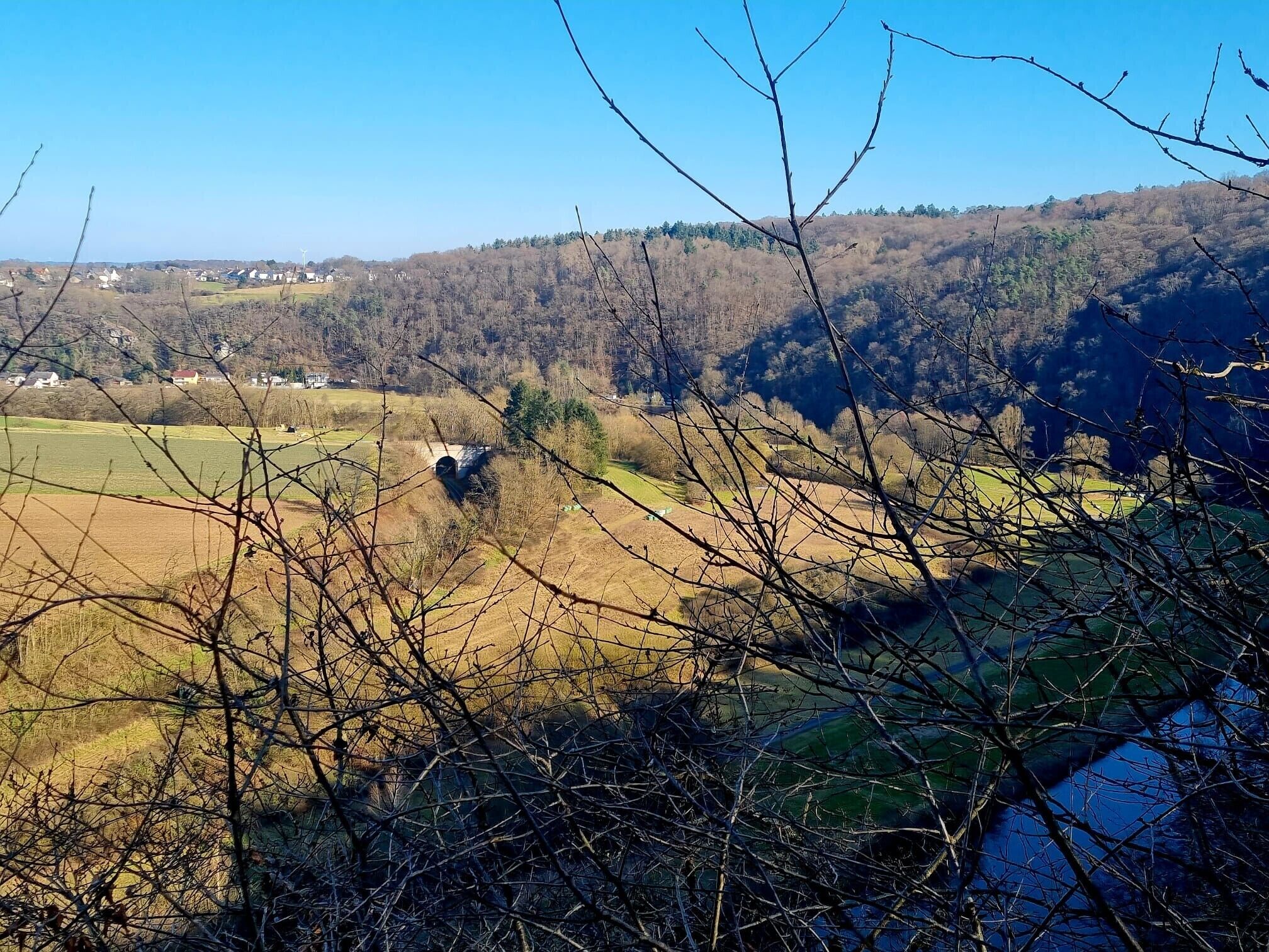 Een landelijk landschap met een brug, velden en een bebost heuvel.