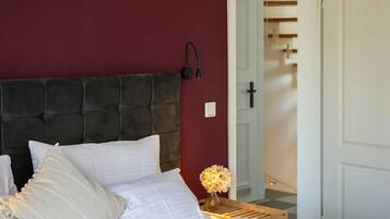 Ein ordentlich bezogenes Bett mit weißen Leinen und einem dunklen Kopfteil, eine an der Wand montierte Lampe und eine Tür, die zu einer Treppe führt.