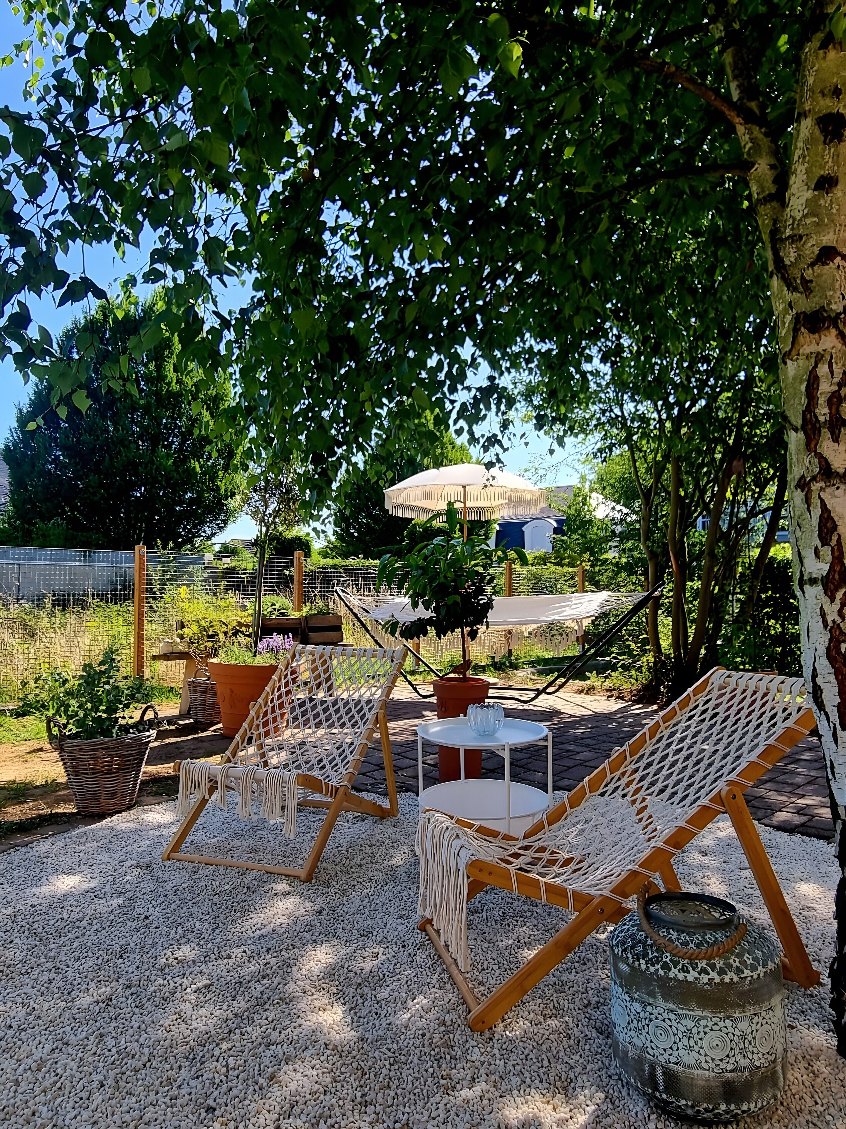 An outdoor seating area with wicker chairs and a table, surrounded by gravel, under a tree.