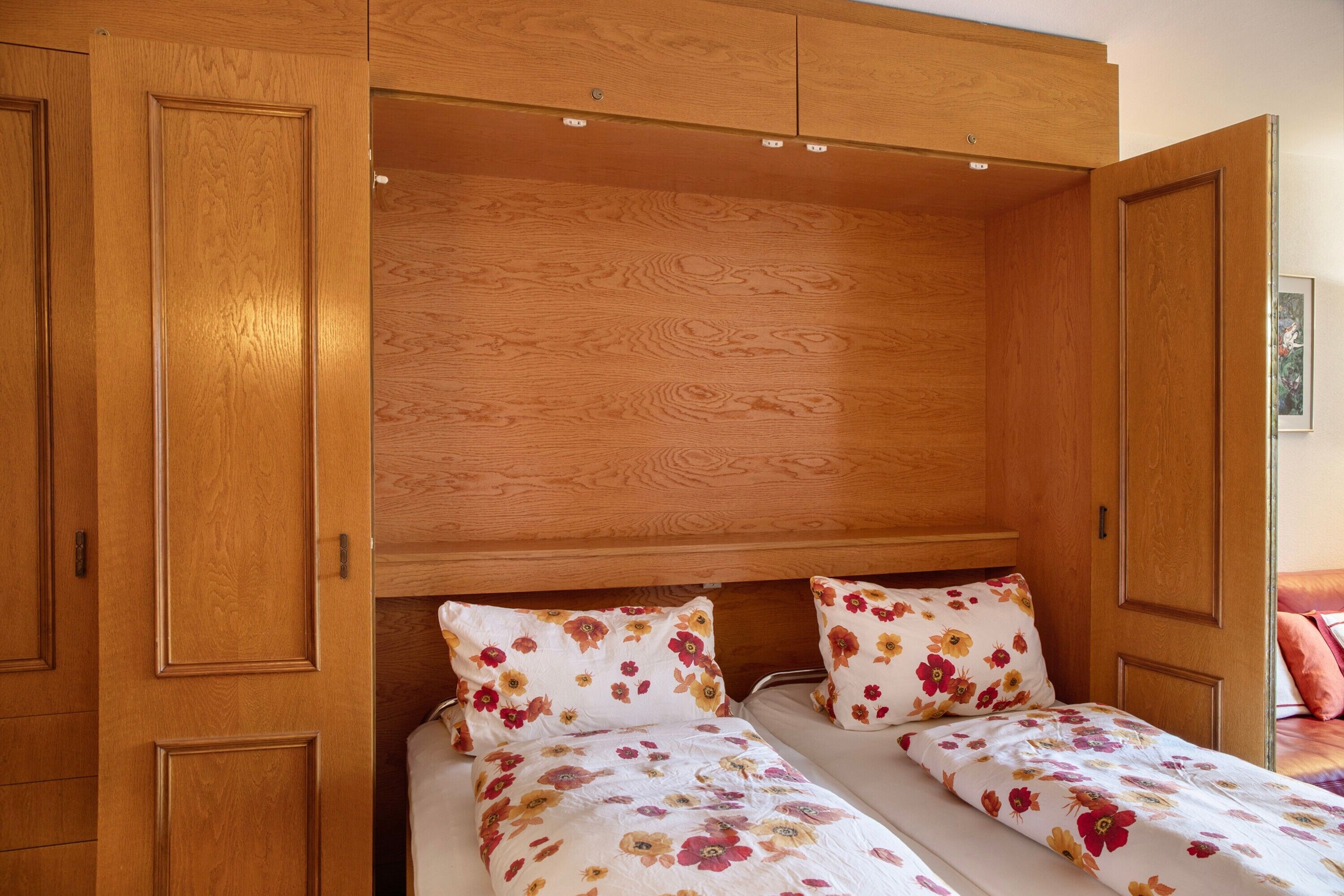 Ein Schlafzimmer mit einem Holzschrank, zwei Betten mit Blumenmuster-Bettwäsche und einem hölzernen Kopfteil.