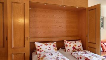 Ein Schlafzimmer mit einem Holzschrank, zwei Betten mit Blumenmuster-Bettwäsche und einem hölzernen Kopfteil.