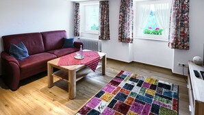 A living room with a red sofa, a wooden coffee table, a colorful rug, and two windows with curtains.