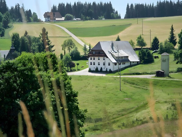 A white building with a sloped roof, surrounded by green fields and trees.
