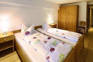 A bedroom with two beds, wooden wardrobe, bedside tables with lamps, and a chair.