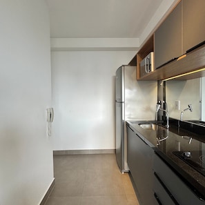 A modern kitchen with a stainless steel refrigerator, black countertop, and wooden cabinets. - Apartamentos Prime-Prox a Oscar Freire (São Paulo)