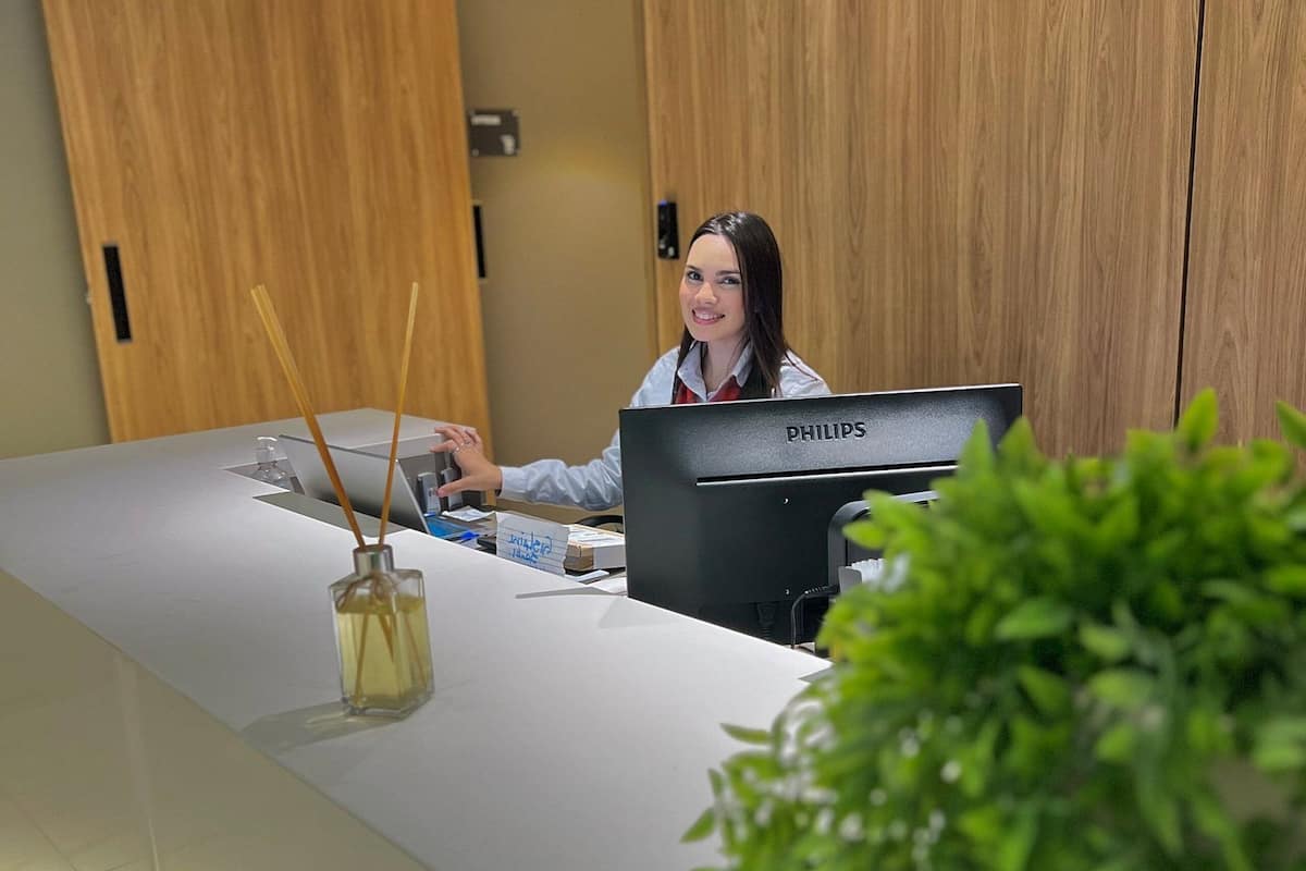 En receptionsdisk med en dator, en flaska handsprit och en liten växt.