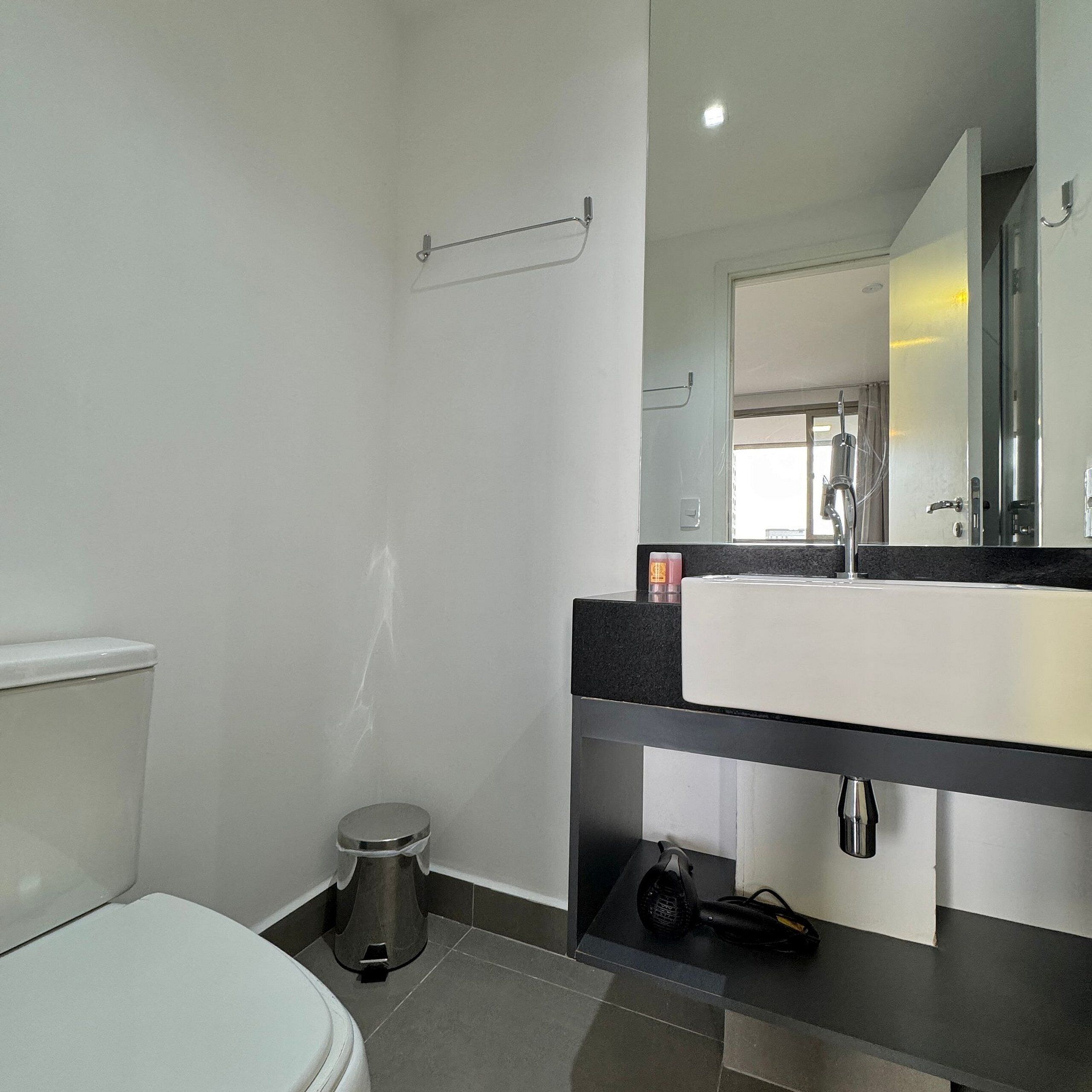 Un baño moderno con inodoro blanco, lavabo negro y un espejo encima.