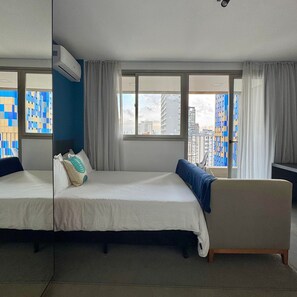 Habitación de hotel con cama, sofá, ventana con cortinas y vista a edificios.