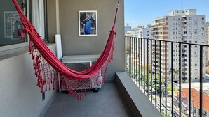 A balcony with a red hammock, a framed picture on the wall, and a view of city buildings. - Apartamentos Prime-Prox a Oscar Freire (São Paulo)