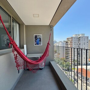 Un balcón con una hamaca roja, un cuadro en la pared y vistas a edificios de la ciudad.
