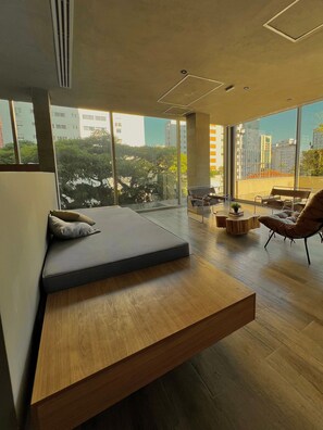 Un salon moderne avec un canapé intégré, une table basse en bois et une vue sur la ville grâce à de grandes fenêtres.