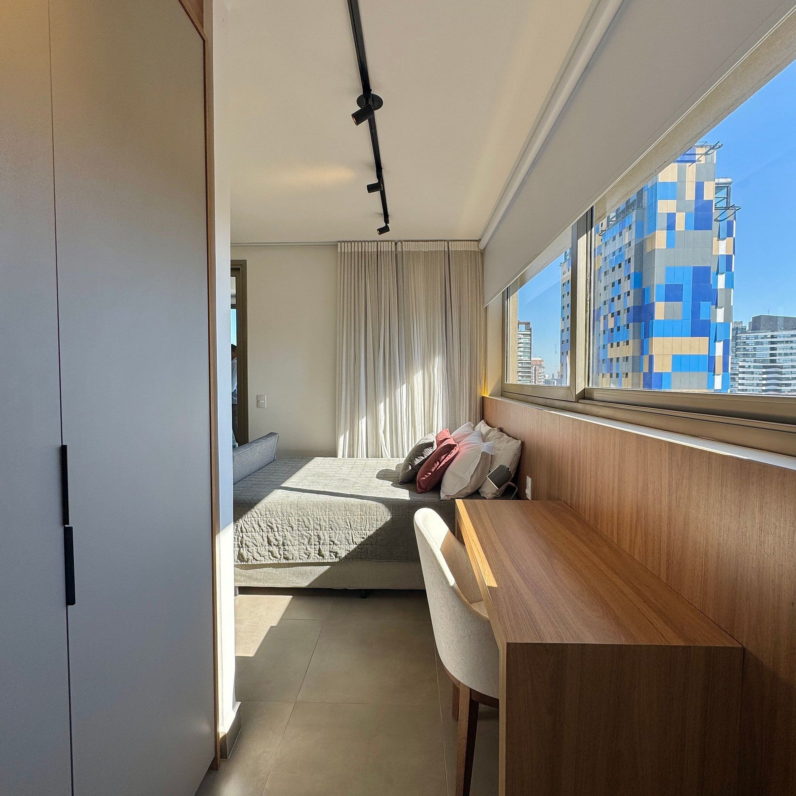 Quarto de hotel moderno com cama, escrivaninha e vista para a paisagem urbana.