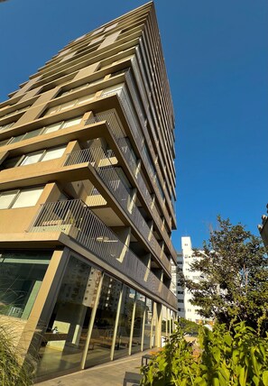 Um edifício moderno de vários andares com varandas, janelas amplas e céu claro.