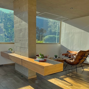 A modern office space with a wooden desk, a leather chair, and a large window offering a view of greenery.