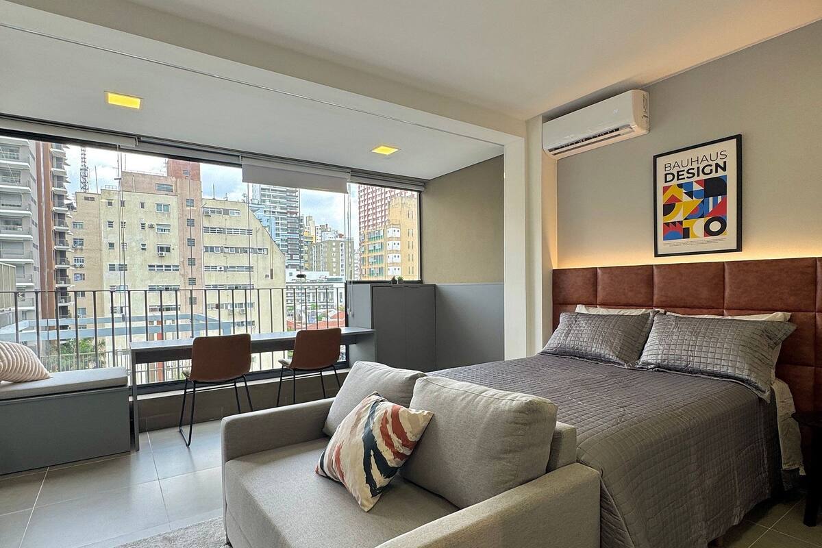Quarto de hotel moderno com uma cama grande, um sofá, uma escrivaninha e vista para a cidade.