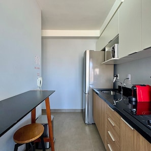 A compact kitchen with a refrigerator, microwave, coffee maker, and a small dining table with a chair. - Apartamentos Prime-Prox a Oscar Freire (São Paulo)