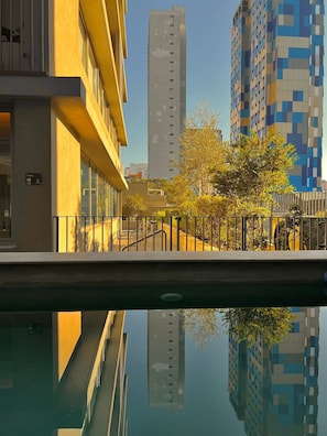A modern building with a reflective pool in the foreground, surrounded by trees and other high-rise buildings.
