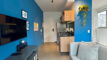 A modern living room with a flat-screen TV, a sofa, and a kitchen area with wooden cabinets.