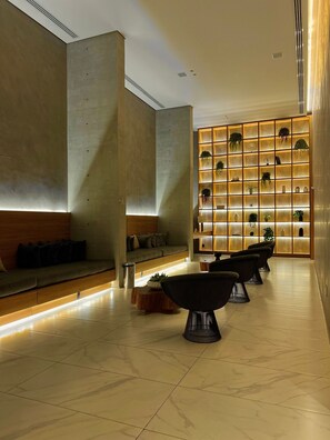 Un hall d’entrée moderne doté d’un espace salon, d’un mur avec des étagères éclairées et d’un design épuré et minimaliste.