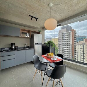 A modern kitchen with a built-in microwave, a stainless steel refrigerator, and a coffee maker. There is a dining table with chairs and a fruit bowl. - Apartamentos Prime-Prox a Oscar Freire (São Paulo)