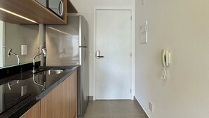 A modern kitchen with a stainless steel refrigerator, wooden cabinets, a black countertop, and a white door. - Apartamentos Prime-Prox a Oscar Freire (São Paulo)