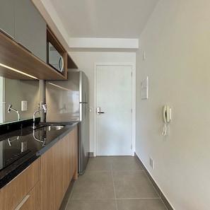 A modern kitchen with a stainless steel refrigerator, wooden cabinets, a black countertop, and a white door. - Apartamentos Prime-Prox a Oscar Freire (São Paulo)
