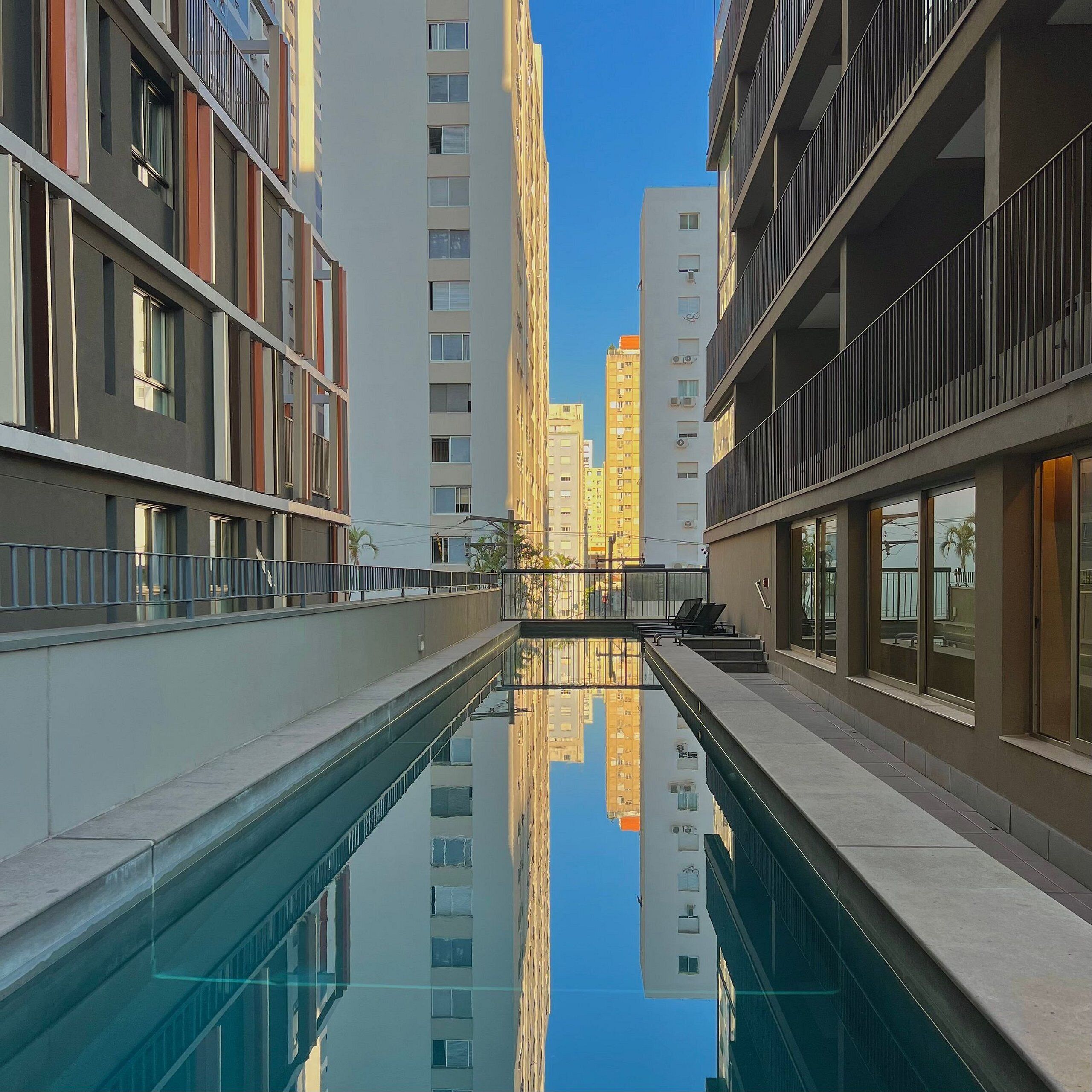 Um edifício moderno com uma piscina refletora em primeiro plano, rodeado por apartamentos altos.