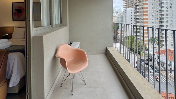 A balcony with a view of a cityscape, a chair, and a bed with a nightstand. - Apartamentos Prime-Prox a Oscar Freire (São Paulo)