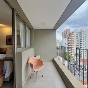 Een balkon met uitzicht op een stadsgezicht, een stoel en een bed met nachtkastje.