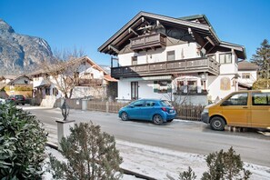 A two-story building with a balcony, a street with cars, and a mountain in the background.