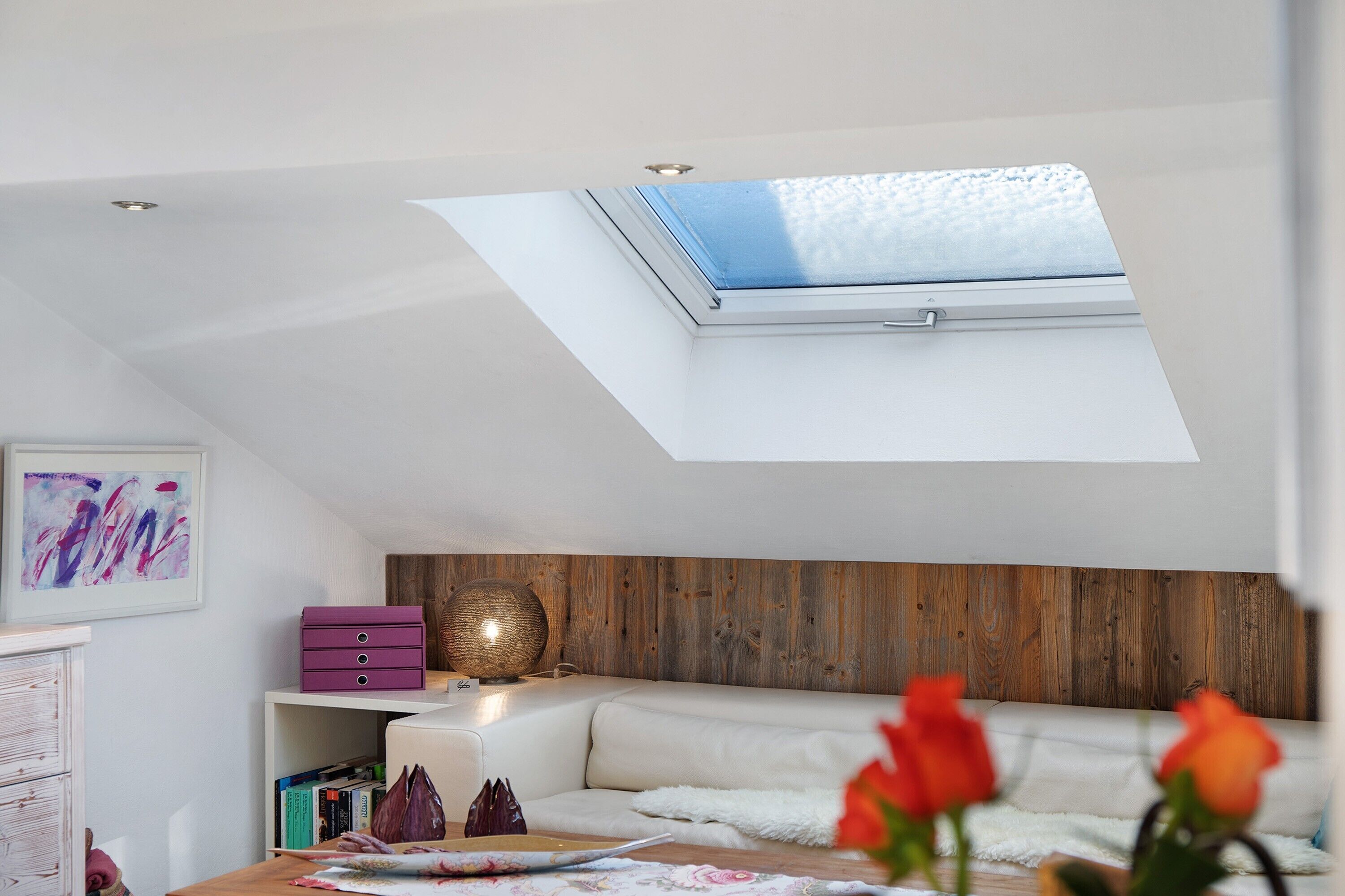 Une pièce dotée d’une lucarne, d’un canapé blanc, d’un mur d’accent en bois, d’un meuble de rangement violet et d’une sphère décorative.