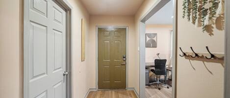 A hallway with a wooden floor, a door, and a desk with a chair.