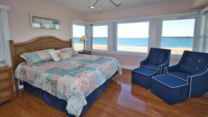 Ein Schlafzimmer mit Bett, Deckenventilator, Nachttisch, Lampe und Blick auf den Strand.