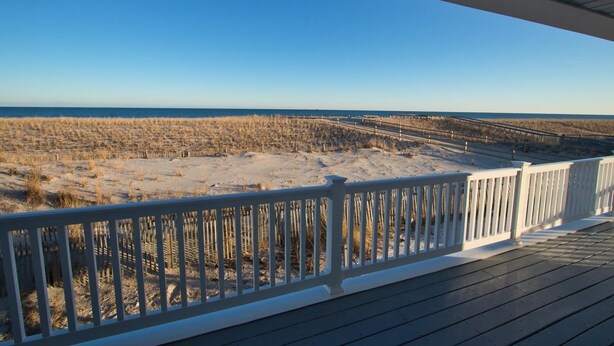 Blick auf einen Strand von einer Holzterrasse mit weißer Geländer.