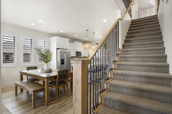 A modern kitchen with white cabinets, a stainless steel refrigerator, and a dining area with a wooden table and chairs.
