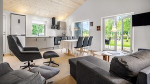 Eine moderne Küche mit Essbereich, ein Wohnzimmer mit grauen Sofas und große Fenster mit Blick ins Freie.
