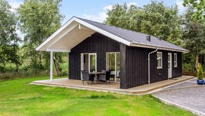 Eine moderne schwarze Holzhütte mit überdachter Terrasse, großen Fenstern und einer Holzterrasse.