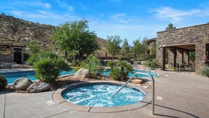 Zona de piscina con un jacuzzi, rodeada de rocas y plantas, y un edificio de piedra al fondo.