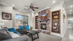 A living room with a fireplace, grey sofa, and a ceiling fan.