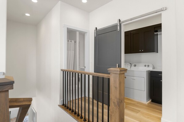 Une cuisine moderne dotée d’un lave-linge encastré, d’un meuble sombre et d’une rambarde d’escalier en bois.